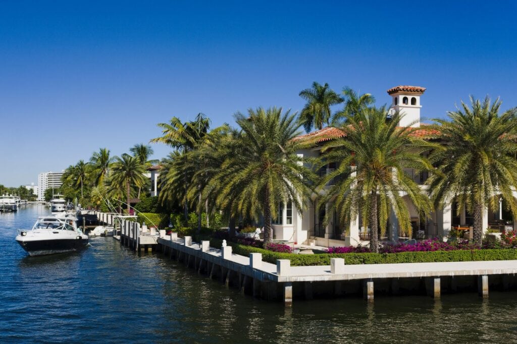 Waterfront estate behind a capped concrete seawall lined with palms